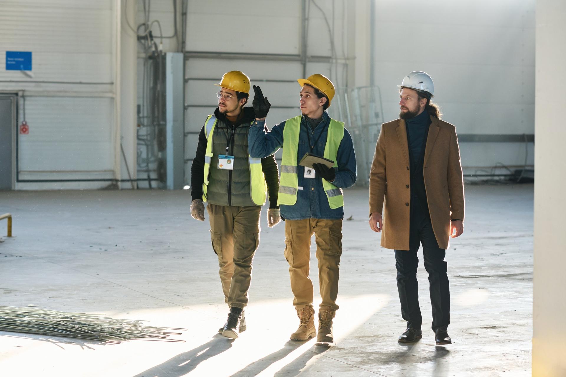 3 people in hard hats walking through an industrial hall